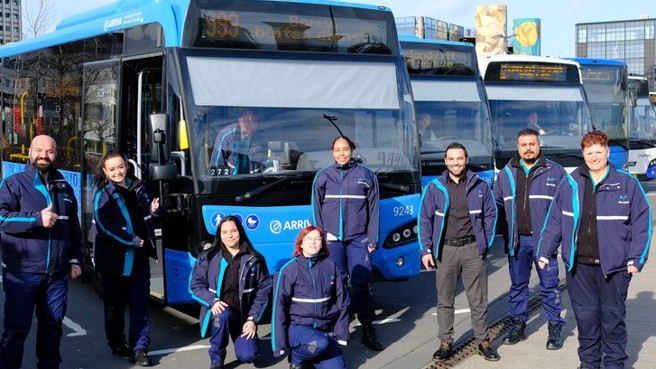 Achter servicemedewerkers poseren in uniform voor zes blauwe Arriva-bussen.
