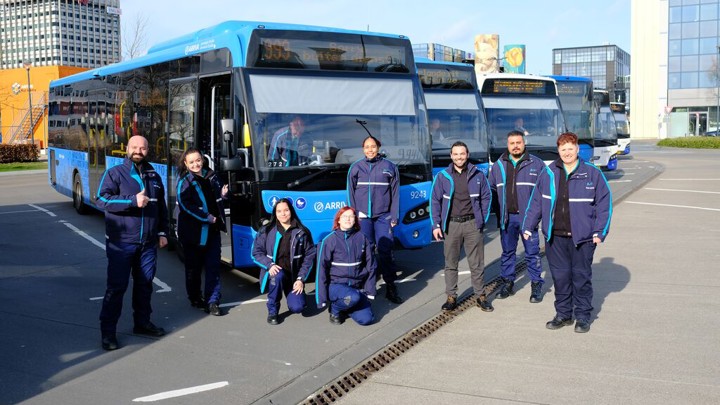 Achter servicemedewerkers poseren in uniform voor zes blauwe Arriva-bussen.