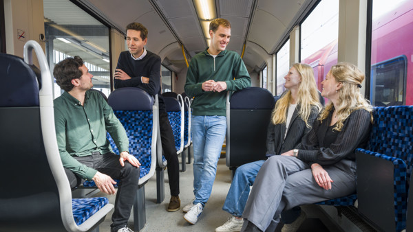  ChatGPT ChatGPT Vier personen in Arriva-trein, twee zittend, twee staand, in levendige discussie. Gekleed in smart casual, duidt op werkgerelateerde reis.