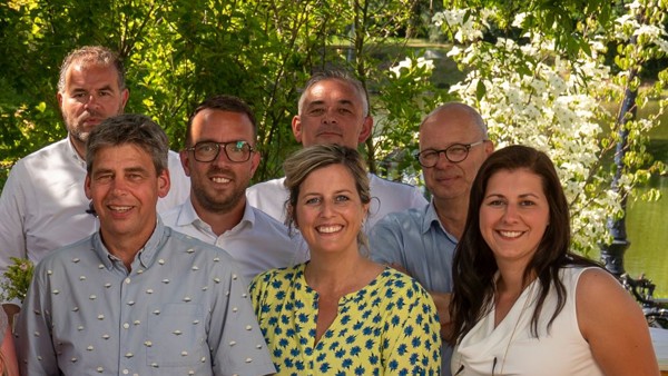 Zeven managers van Arriva staan op een zomerse dag in een groene omgeving en kijken lachend de camera in.