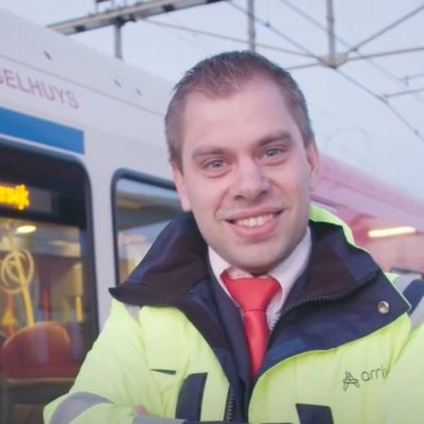 Glimlachende mannelijke treinmachinist staat voor rood-witte Arriva trein.