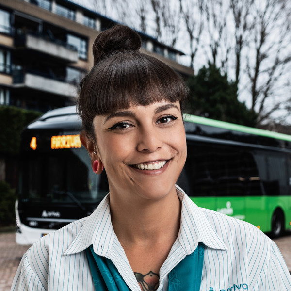 Buschauffeur Pauline staat lachend voor haar Arriva-bus en draagt een Arriva-overhemd.