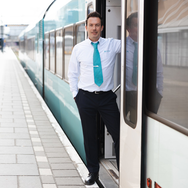 Machinist Mark Dorenbos staat in een van de deuropeningen van zijn Arriva-trein terwijl die bij het perron stilstaat. Machinist Mark Dorenbos staat in een van de deuropeningen van zijn Arriva-trein terwijl die bij het perron stilstaat.