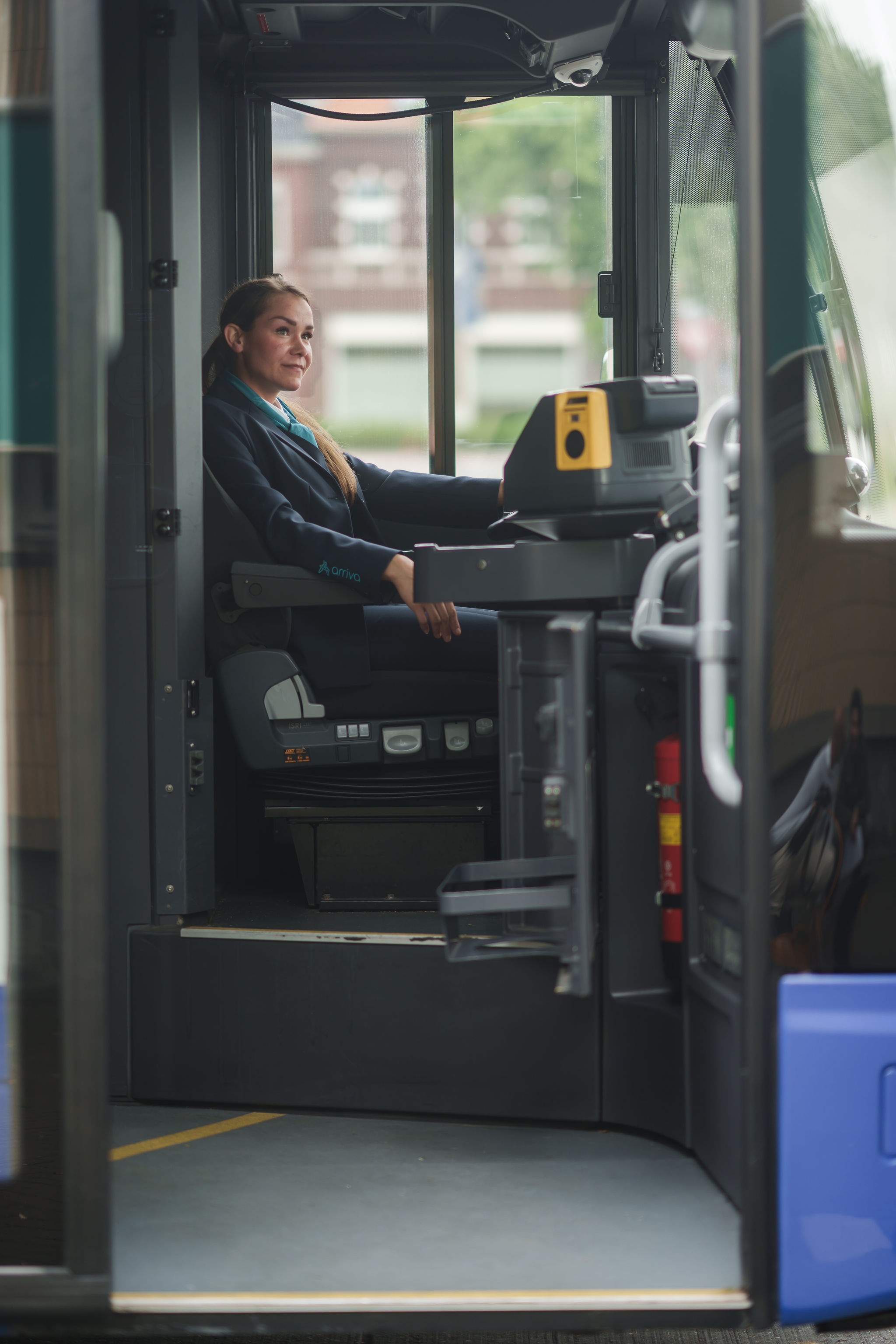 Een buschauffeur van Arriva zit in uniform achter het stuur van een stilstaande bus en kijkt dromerig in de verte.
