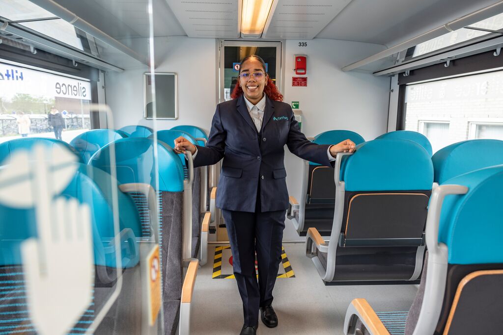  Een vrouwelijke conducteur staat tussen de stoelen in een Arriva trein.
