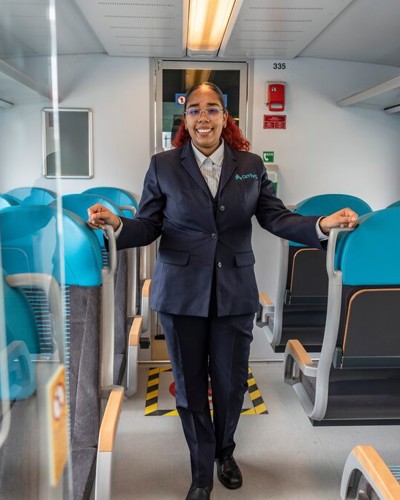 Een vrouwelijke conducteur staat tussen de stoelen in een Arriva trein. Een vrouwelijke conducteur staat tussen de stoelen in een Arriva trein.