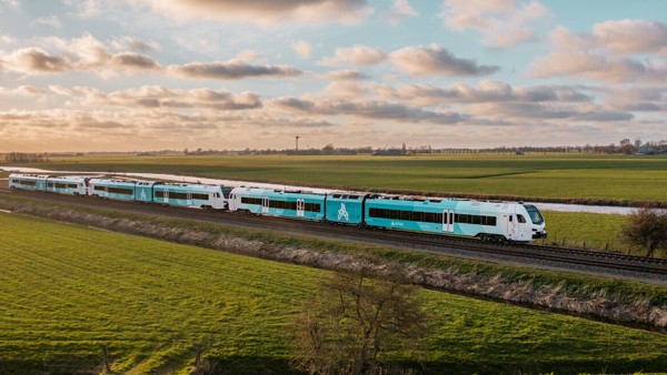 Een blauw-witte Arriva-trein rijdt over het spoor tussen weilanden met een ondergaande zon en een prachtige wolkenlucht.