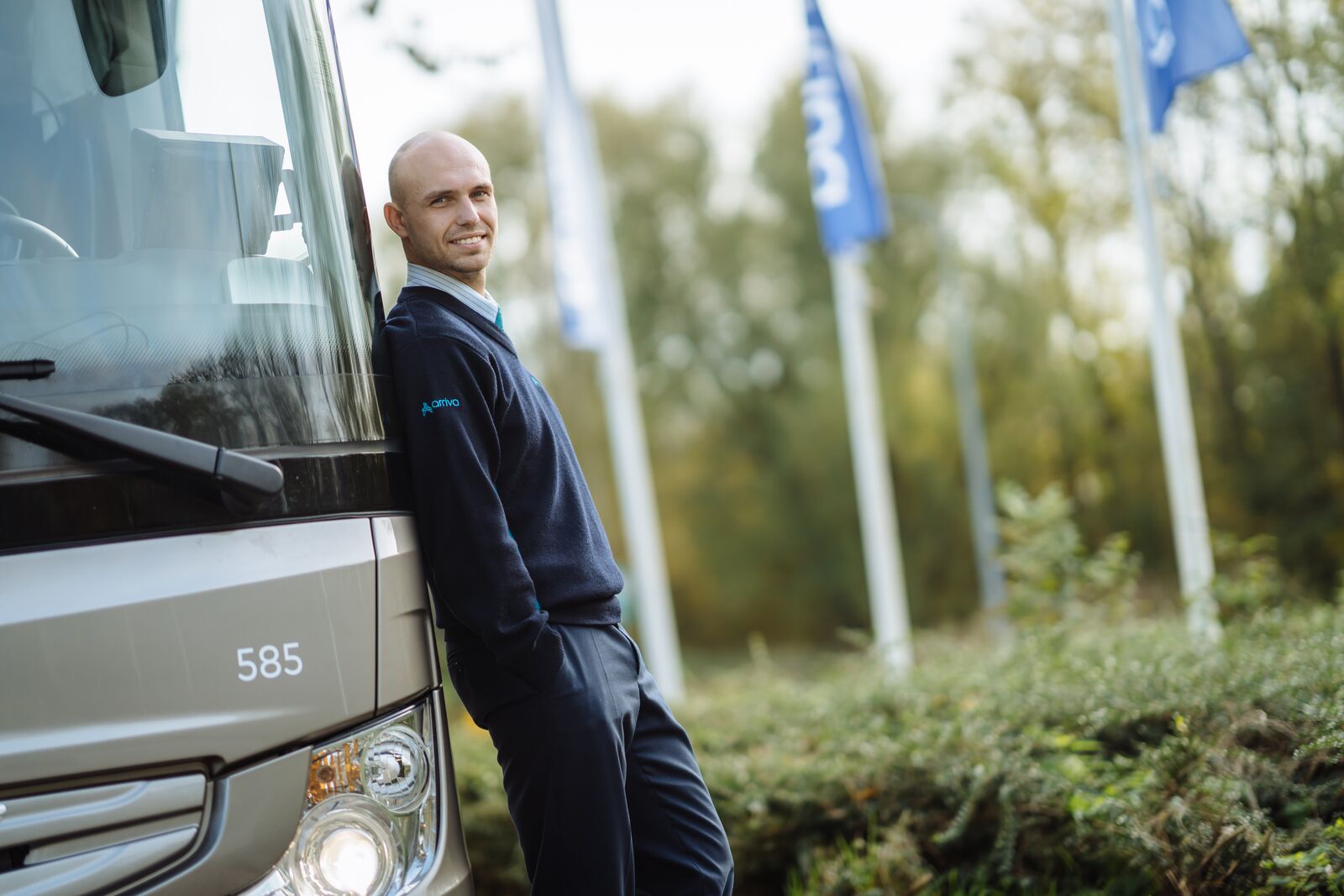 Chauffeur van Arriva leunt relaxt tegen touringcar.