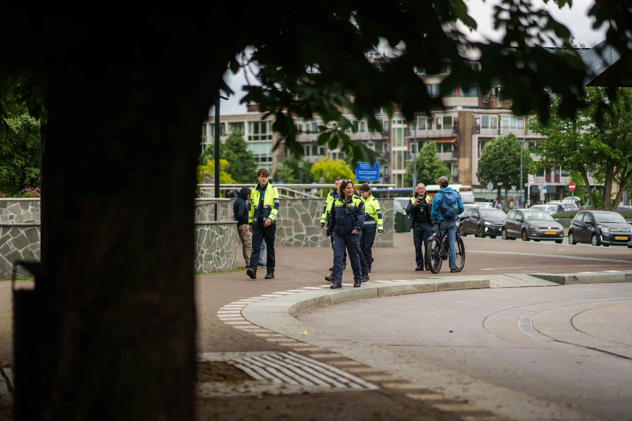 Een groep veiligheidsmedewerkers in uniform loopt buiten over een trottoir, met stedelijke gebouwen en geparkeerde auto’s op de achtergrond.