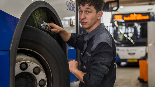 Monteur controleert met een zaklamp de banden van een Arriva bus op de werkplaats.