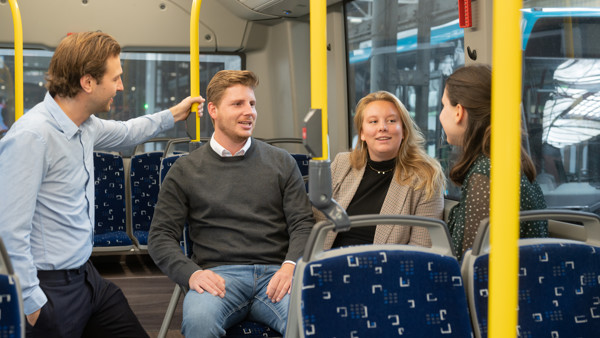 Vier jonge collega's staan en zitten in een Arriva-bus en praten met elkaar.