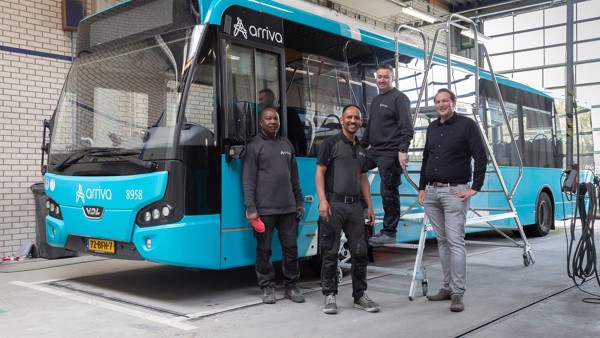 Vier mannen vormen een team voor een blauwe Arriva-bus in de werkplaats en glimlachen.