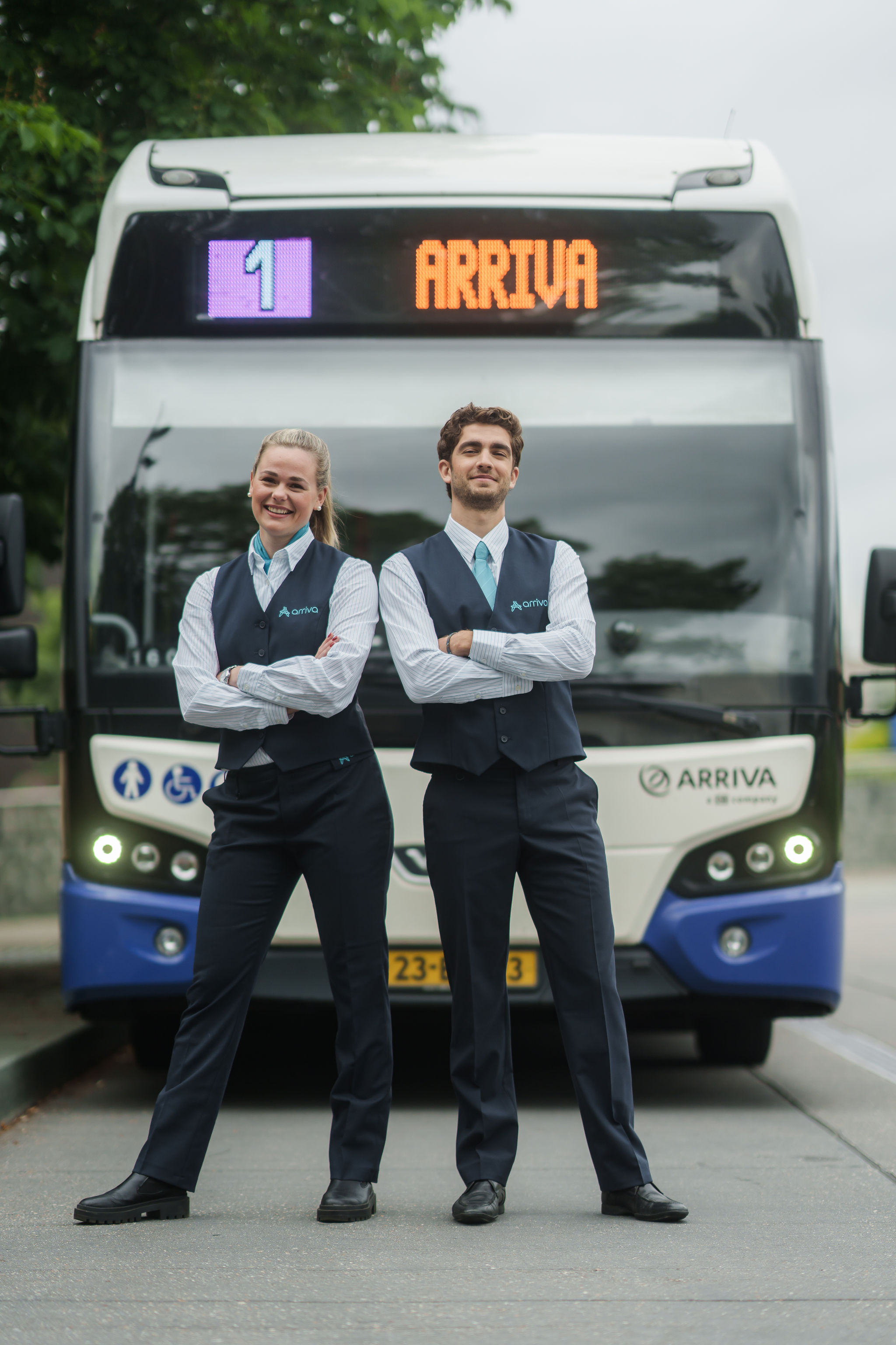 Twee chauffeurs in hun Arriva-uniform staan lachend voor een bus met lijnnummer 1 en Arriva erop.