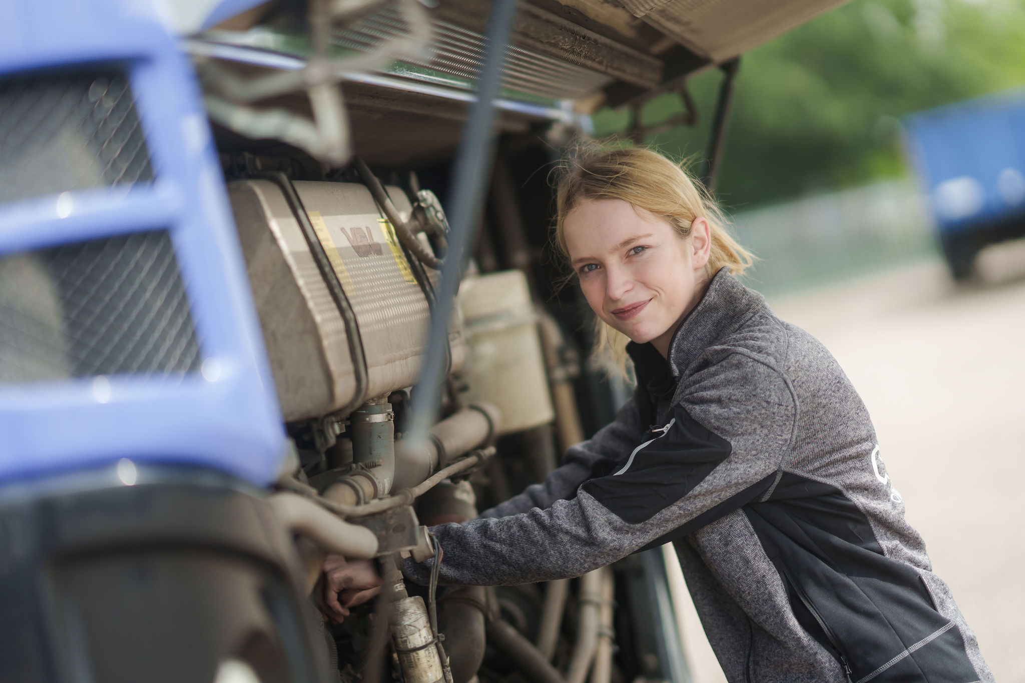 Jonge monteur van Arriva kijkt glimlachend naar camera terwijl ze werkt aan de motor van een bus.