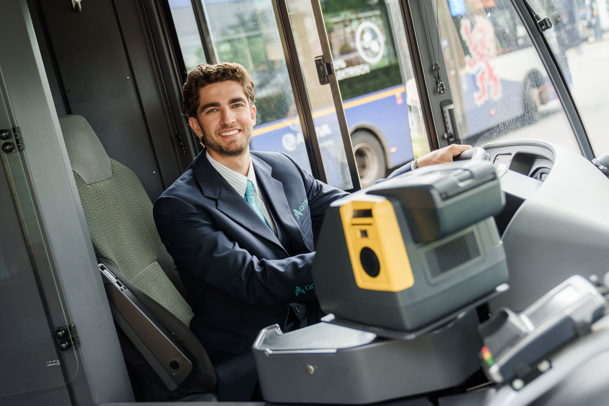 Een buschauffeur van Arriva zit in uniform en breed lachend achter het stuur van een bus.