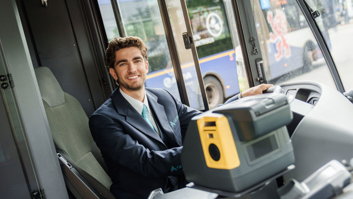 Een buschauffeur van Arriva zit in uniform en breed lachend achter het stuur van een bus. Een buschauffeur van Arriva zit in uniform en breed lachend achter het stuur van een bus.