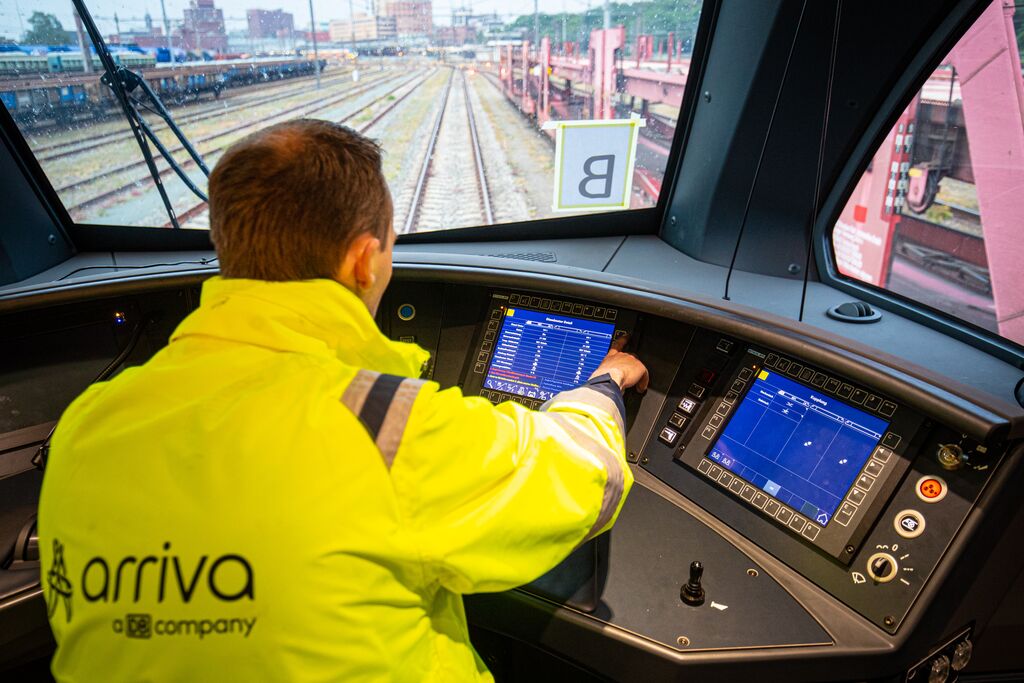 Een mannelijke machinist in uniform zit in de cabine, kijkt uit over het spoor en bestuurt de trein.