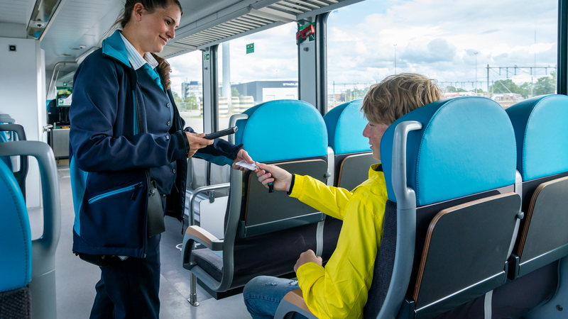 Vrouwelijke steward van Arriva geeft OV-chipkaart terug aan jonge reiziger in gele jas die in de trein zit. Vrouwelijke steward van Arriva geeft OV-chipkaart terug aan jonge reiziger in gele jas die in de trein zit.