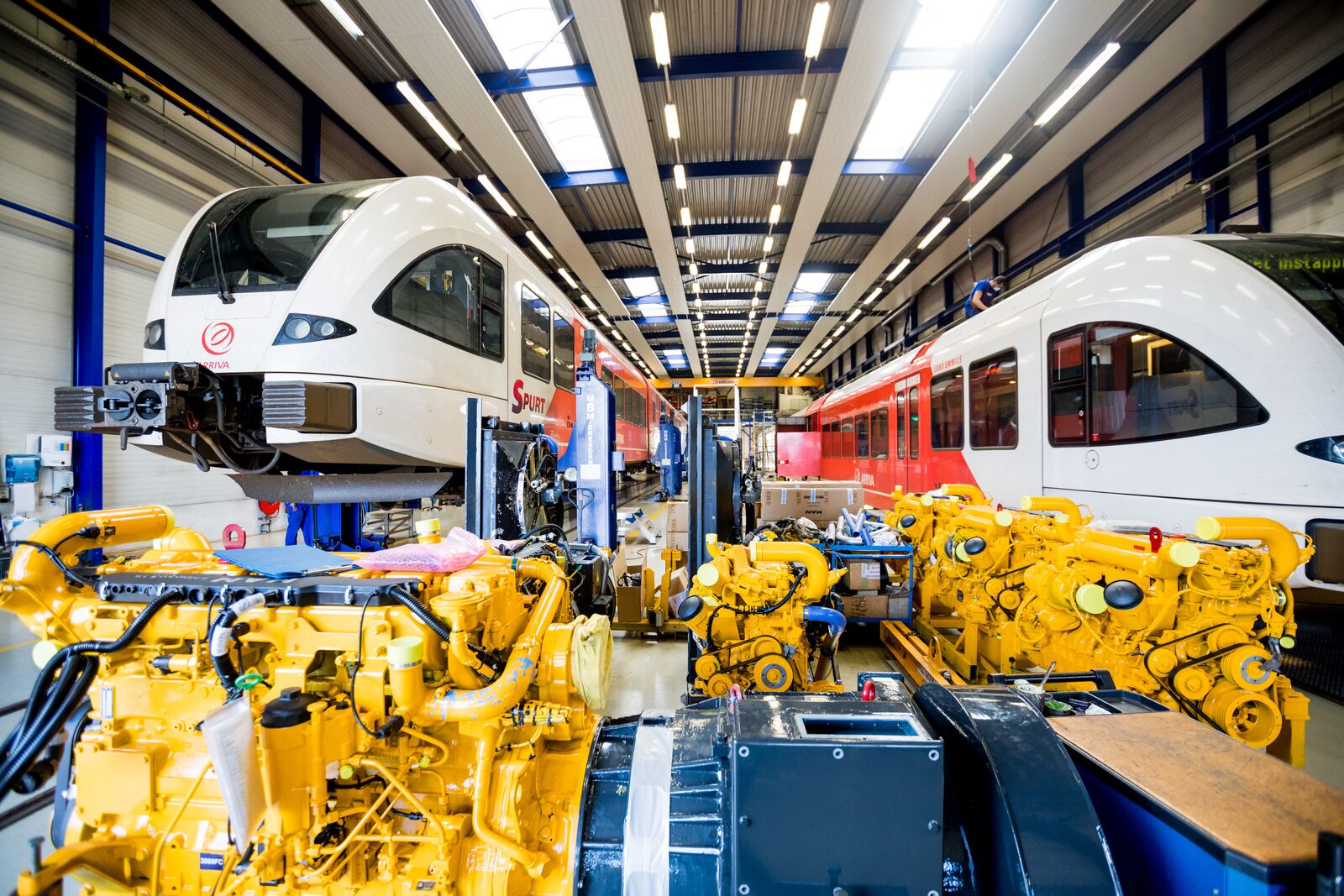 Twee Arriva treinen in een werkplaats met gele machines op de voorgrond.