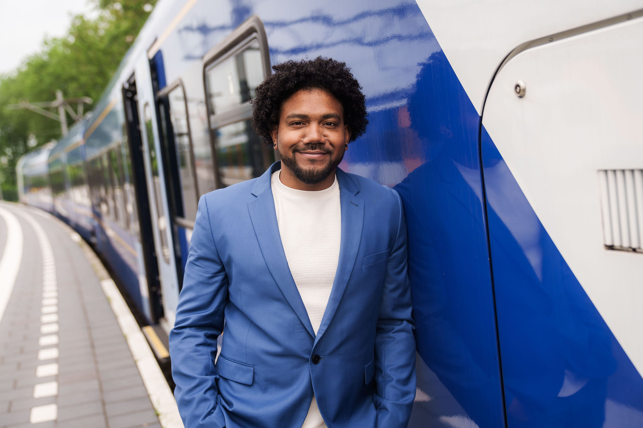 Een teammanager van Arriva staat in blauw pak en glimlachend bij een blauw-witte trein.