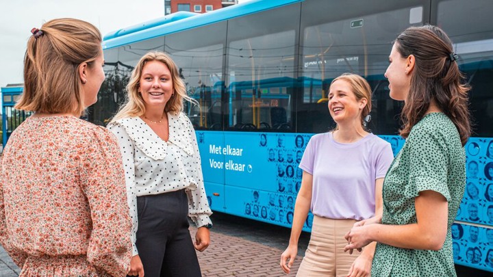 Vier jonge vrouwelijke collega's overleggen lachend met elkaar, op de achtergrond staan blauwe Arriva-bussen.