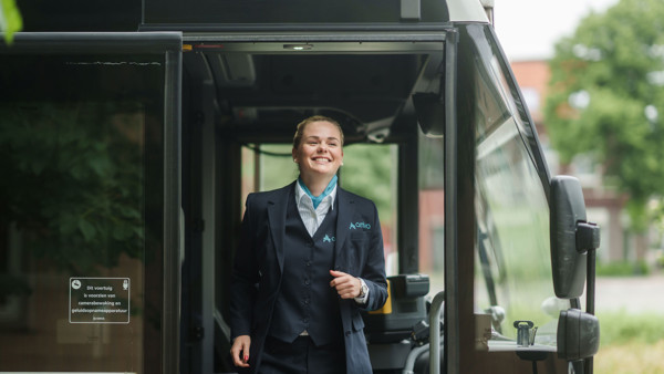 Een lachende buschauffeur in opleiding in Arriva-uniform stapt uit een bus, klaar om aan het werk te gaan. Een lachende buschauffeur in opleiding in Arriva-uniform stapt uit een bus, klaar om aan het werk te gaan.