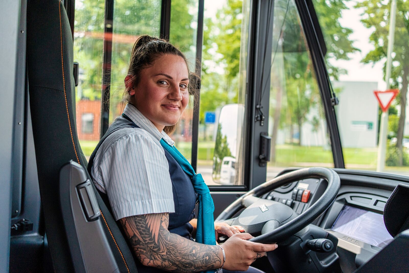 Buschauffeur Kelly van Arriva zit relaxed achter het stuur van haar bus en kijkt achterom naar haar reizigers.