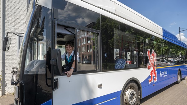 Een glimlachende vrouwelijke busschauffeur kijkt uit het raam van een Arriva bus, terwijl ze achter het stuur zit.