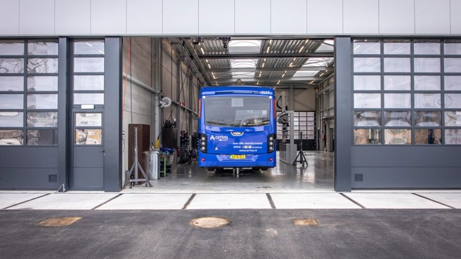 Een blauwe Arriva bus in de opening van een werkplaats met hoge deuren.
