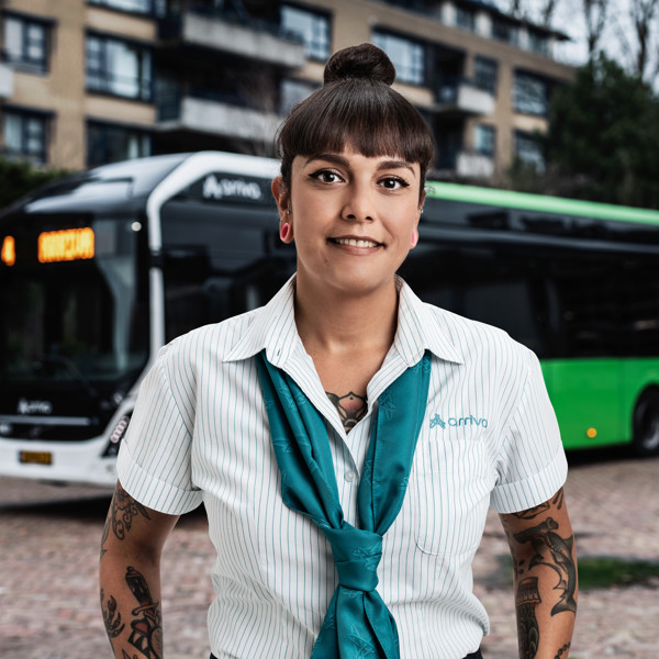 Chauffeur Pauline staat in haar Arriva-uniform voor een groenwitte Arriva-bus.