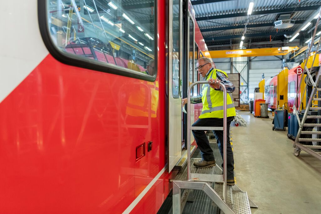 Rood-witte Arriva-trein in werkplaats, monteur in geel hesje stapt de trein in.