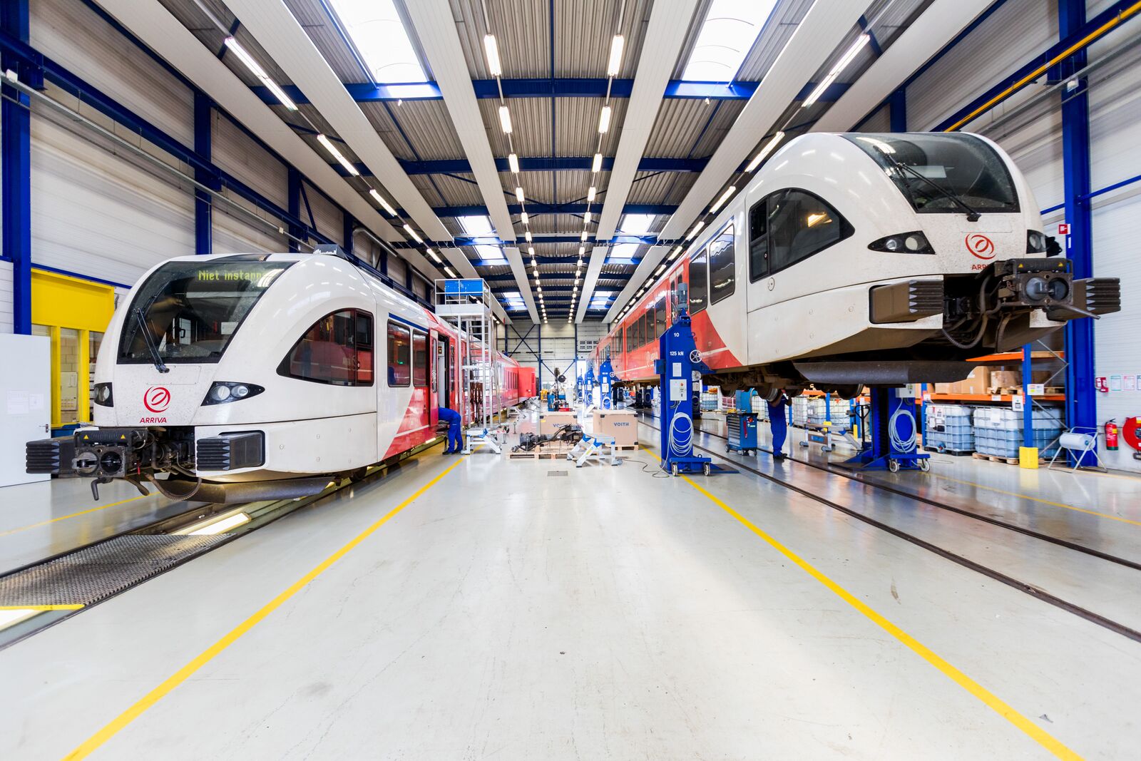 Twee wit-rode Arriva-treinen in een goed verlichte werkplaats.