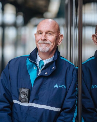 Een mannelijke conducteur met een Arriva-jas leunt ontspannen tegen de zijkant van een Arriva-trein. Een mannelijke conducteur met een Arriva-jas leunt ontspannen tegen de zijkant van een Arriva-trein.