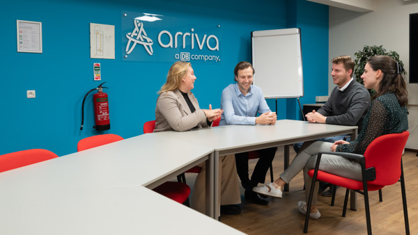 Vier jonge collega's van Arriva vergaderen in een ruimte met Arriva op de wand en een flipboard op de achtergrond.