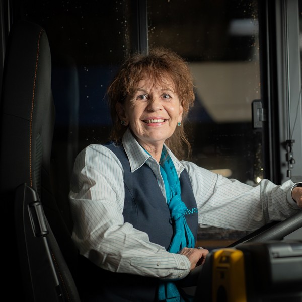 Buschauffeur Marion zit in haar Arriva-uniform lachend achter het stuur van een bus. Buschauffeur Marion zit in haar Arriva-uniform lachend achter het stuur van een bus.