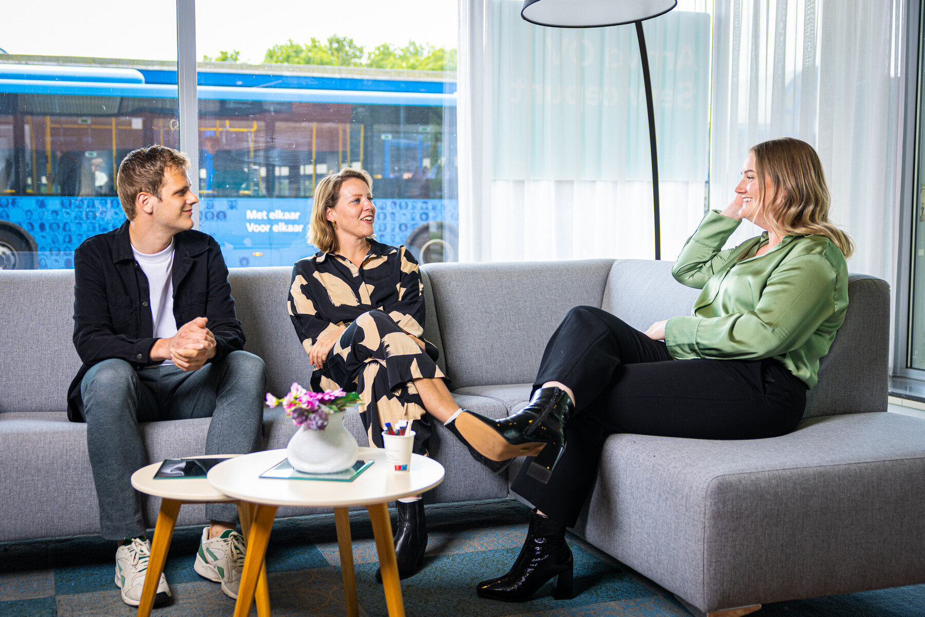 Een recruiter van Arriva is in gesprek met twee mensen. Ze zitten op een grijze bank.