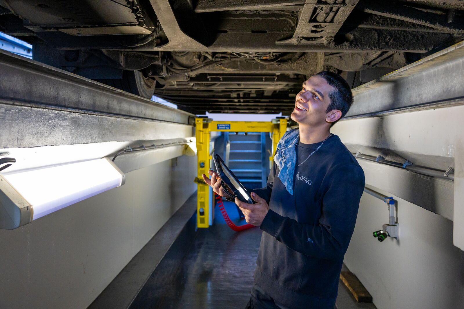 Monteur staat op de brug onder een Arriva-bus met een tablet in zijn hand.