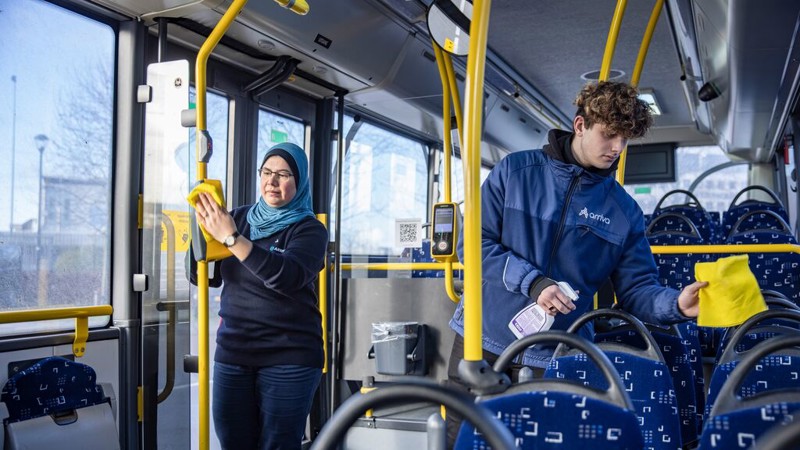 Twee service medewerkers, een jongen en een vrouw, zijn bezig met schoonmaken in een Arriva-bus.