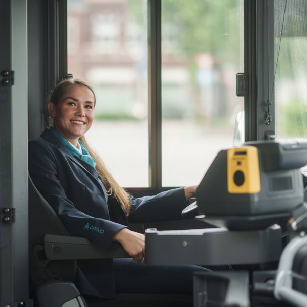 Buschauffeur zit achter stuur van een bus en kijkt lachend opzij in de camera. Buschauffeur zit achter stuur van een bus en kijkt lachend opzij in de camera.